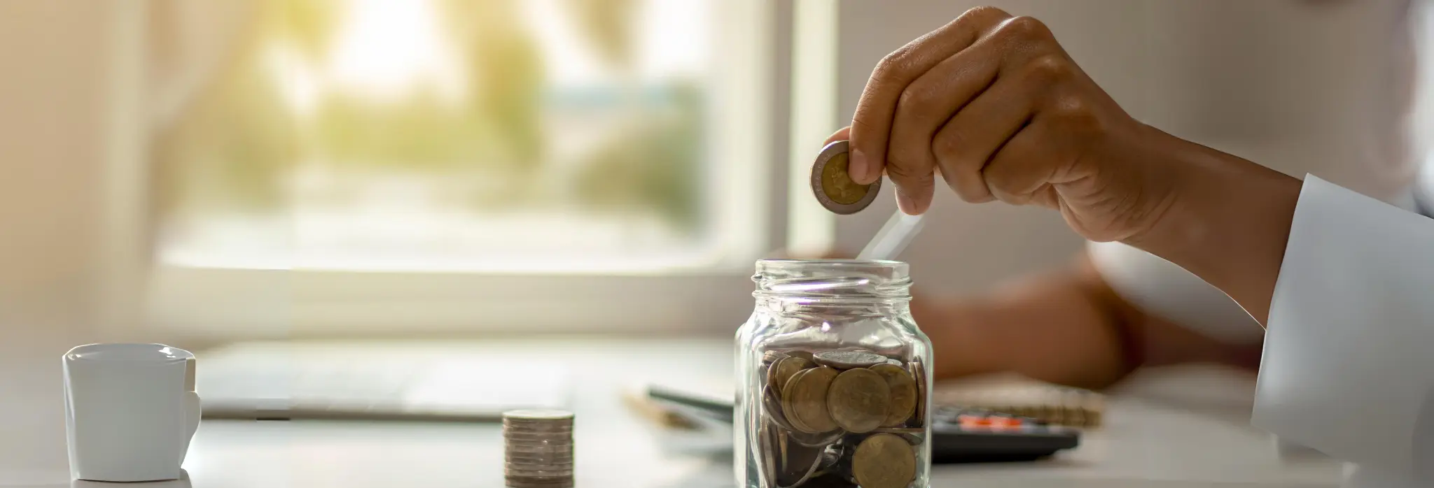 Χέρι τοποθετεί νόμισμα των 2€ σε βαζάκι με κέρματα.