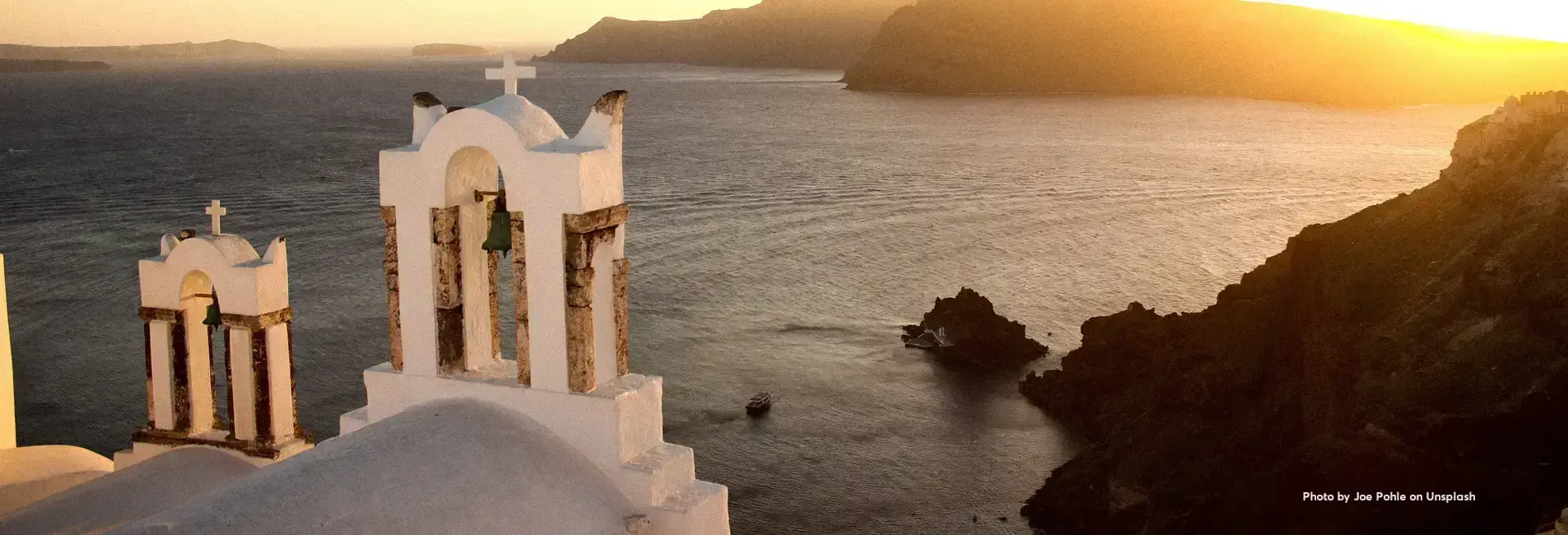 Λευκό καμπαναριό εκκλησίας με σταυρούς μπροστά στη θάλασσα.