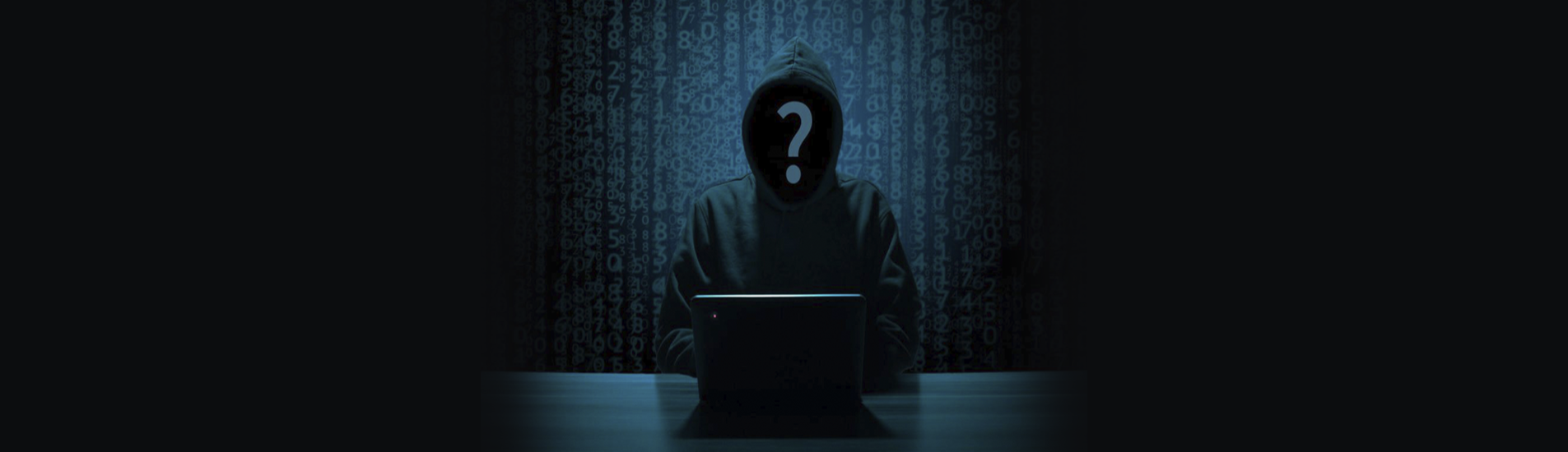 Hacker με κουκούλα σε σκοτεινό δωμάτιο μπροστά από laptop